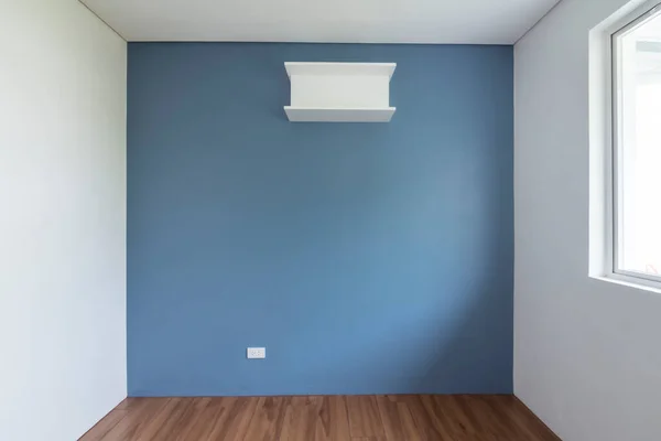 A bare room with a baby blue painted wall, plain white side and ceiling, wood parquet flooring and a single ledge. Unfurnished interior good for mockup.