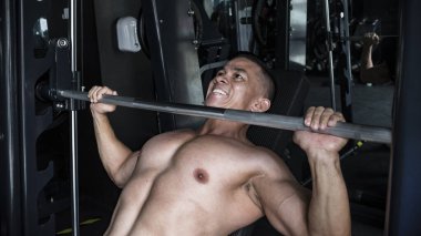 Çıplak göğüslü bir adam, spor salonunda ya da fitness merkezinde Smith Machine 'e halterli ağırlık kaldırıyor. Bölgedeyim ve göğüs kası eğitimi alıyorum..