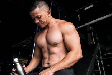 Orta yaşlı kaslı bir erkek spor salonunda ya da fitness kulübünde göğüs egzersizi yaparken kısa bir süre dinlenir..