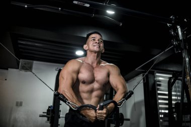 Yakışıklı ve atletik Asyalı bir adam kablolu yayın yapıyor. Spor salonunda göğüs egzersizi..