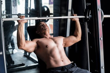 Antrenman ve antrenman sahnesi - 40 yaşında üstsüz, fit bir Asyalı Smith Machine 'in üzerinde benç basar.