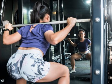 Formda Asyalı bir kız bir demirci makinesine çömeliyor. Spor salonunda ya da fitness kulübünde antrenman yapıyorum..