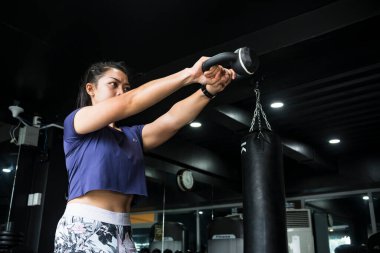 Genç Asyalı bir kız spor salonunda iki elle kettlebell sallıyor. Omuzlarını çalıştırmak ya da çaprazlama yapmak. Düşük açılı çekim.