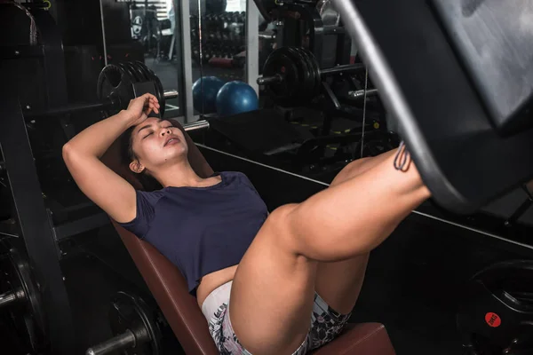 A tired and burned out asian girl on the leg press machine at the gym. Wanting to give up, feeling unmotivated and fatigued.