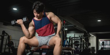 Kaslı ve kaslı bir genç spor salonunda kıvırcık saçlar yapıyor. Spor salonunda bisepsleri çalıştırıyorum..