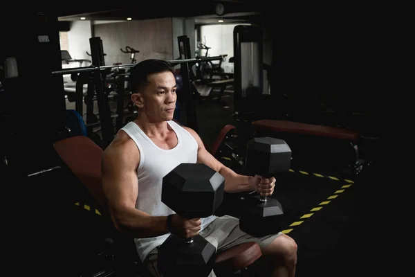 An athletic asian man lift some heavy hex dumbbells, preparing mentally to work out chest and shoulders.