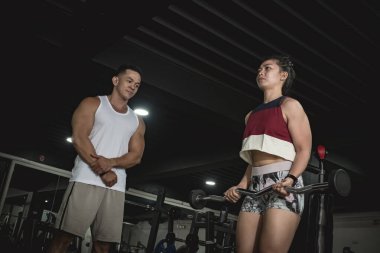 Bir jimnastik hocası halter kıvırırken müşterilerinin formlarını gözlemler. Spor salonunda kişisel eğitim..