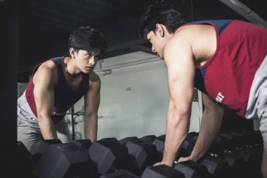 Orta seviyede kas gelişimine sahip genç bir adam ciddi bir çalışma için bölgeye giriyor. Halter rafının yanında..