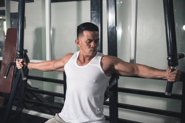 Kaslı ve yakışıklı Asyalı bir adam göğüs sineği makinesinde uçuyor. Spor salonunun güvertesi olarak da bilinir..