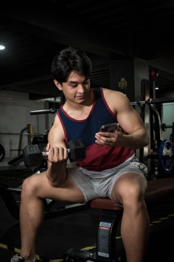 Yakışıklı, genç Asyalı bir adam antreman yaparken telefonuyla video izliyor. Dikkati dağılmış ya da çoklu görev.