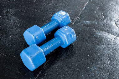 Spor salonunun ya da sağlık kulübünün kauçuk döşeli zemininde duran bir çift mavi, sert plastik uğursuz halter..