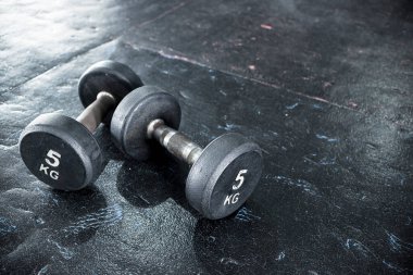 Spor salonunda ya da fitness merkezinde giyilmiş siyah kauçuk taban panellerine orta halli bir çift dambıl..