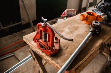 Turuncu bir çelik boru ahşap bir derme çatma masaya sabitlenmiş. Aynı masada büyük bir cırcırböceği yatıyor. İnşaat halindeki bir binanın şantiyesinde.