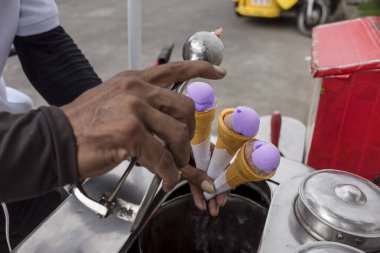 A Sorbetero scoops some ube and chocolate sorbetes, a traditional ice cream popular in the Philippines clipart