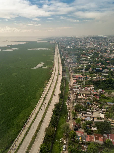 Aerial of C6 Highway, also known as Southeast Metro Manila Expressway, traversing a section of Bicutan and Laguna Lake. Laguna de Bay on the left is infested with a bloom of invasive water hyacinths.