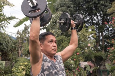 A fit, focused, middle aged Filipino male attempts to do a full set of shoulder dumbbell presses. Middle closeup shot.