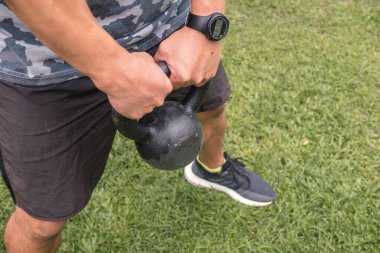 İsimsiz bir adam elinde kettlebell salıncakları yapmaya hazır bir çaydanlık tutuyor. Dışarıda çalışıyorum..