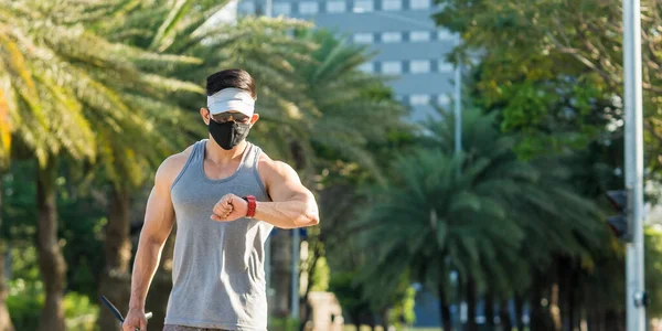 An asian guy checks the time and distance walked while strolling around the city for fitness and health purposes. Wearing a face mask, new normal scene outdoors.