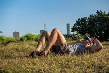 Atletik ve formda Asyalı bir adam şehrin yakınındaki bir açık arazide çimlerin üzerinde mekik çekiyor. Karın egzersizi ya da açık havada beden eğitimi...