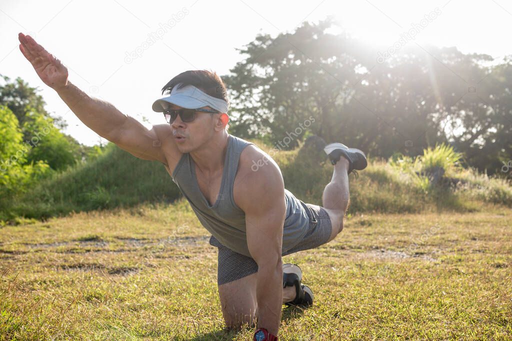 An athletic asian man performs bird dogs on the grass of an open field. Lower back and ab workout.