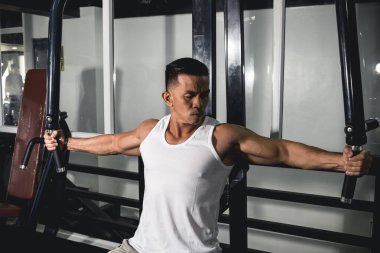 Kaslı bir Asyalı spor salonundaki göğüs sineği makinesini kullanıyor. Göğüs kasları çalışıyor..