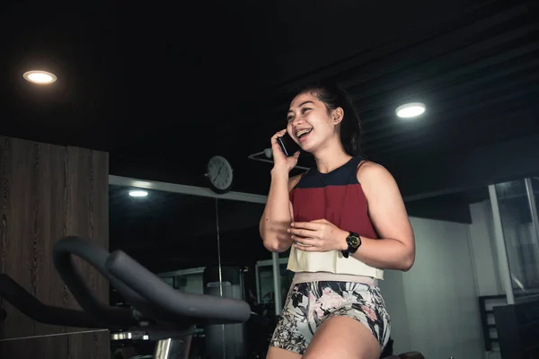 Sporty Asian Woman Talks Her Friend Phone While Stationary Bike — Stock Photo, Image