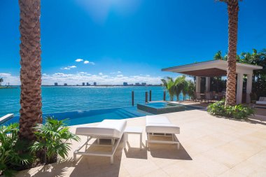 Miami Plajı - Bir çift güneşlenme sandalyesi ve lüks bir evde sonsuz bir havuz. Tipik Güney Florida tasarımı.