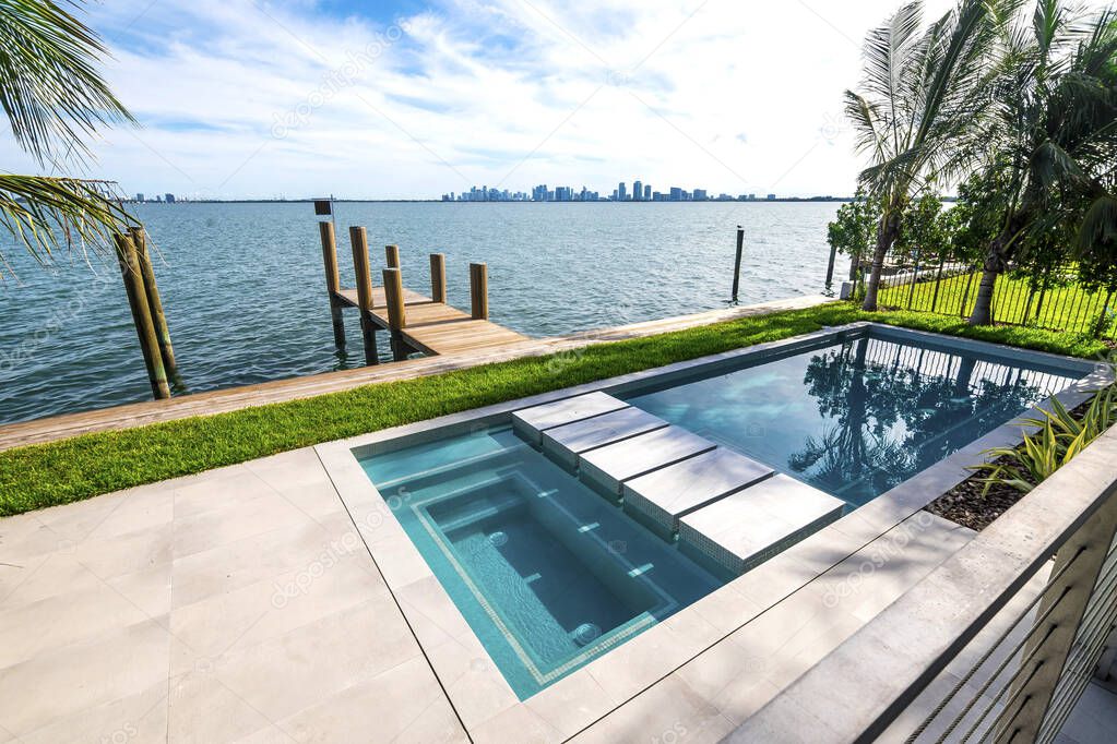 Miami Beach - A modern swimming pool near a small wooden dock overlooking the bay. Luxury residence in South Florida.