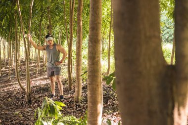 Formda ama yorgun Asyalı bir adam mola verir ve bir patika koşusu sırasında ormanın ortasında bir ağaca yaslanır. Kardiyo ve macera kavramları.