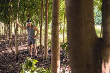 Formda ama yorgun Asyalı bir adam mola verir ve bir patika koşusu sırasında ormanın ortasında bir ağaca yaslanır. Kardiyo ve macera kavramları.