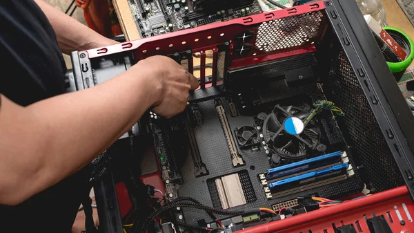 A computer IT technician opens up a desktop computer and inspect its parts while holding a small screwdriver. Upgrading, troubleshooting or replacing PC parts.