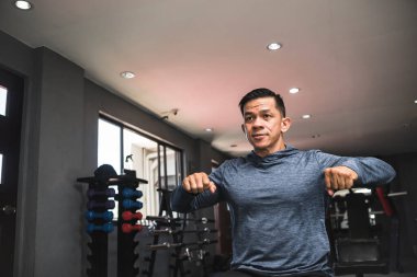 Sweatshirt giyen yakışıklı Asyalı bir adam spor salonunda antrenman yapmaya hazırlanırken göğsünü gerer..