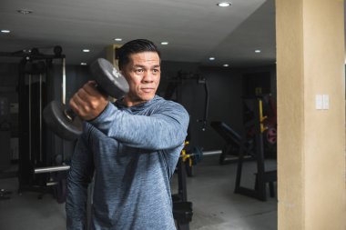 Sweatshirt 'lü yakışıklı bir Asyalı ters bir halter kaldırıyor. Anterior deltoid omuz egzersizi ve spor salonunda eğitim..