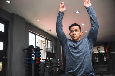 40 'lı yaşlarda Asyalı bir adam spor salonunda antrenman yapmak için omuzlarını esnetiyor..