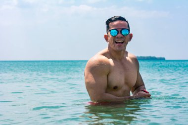 Güneş gözlüğü takan kaslı ve atletik Asyalı bir adam denize dalarken iyi vakit geçirir. Yaz zamanı plaj için vücut golleri.