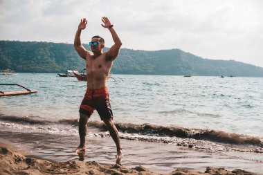 Asyalı fitness elemanı atlama, yıldız atlaması ya da deniz kenarında burpee egzersizi yapıyor. Sahilde sağlıklı bir yaşam tarzı..