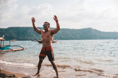 Asyalı fitness elemanı atlama, yıldız atlaması ya da deniz kenarında burpee egzersizi yapıyor. Sahilde sağlıklı bir yaşam tarzı..