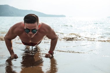 Formda ve atletik Asyalı bir adam sahilde şınav çeker. Manzaralı deniz manzaralı bir yerde çalışıyor ve antrenman yapıyor. Kopyalama alanı ile çekilen ışığa karşı.