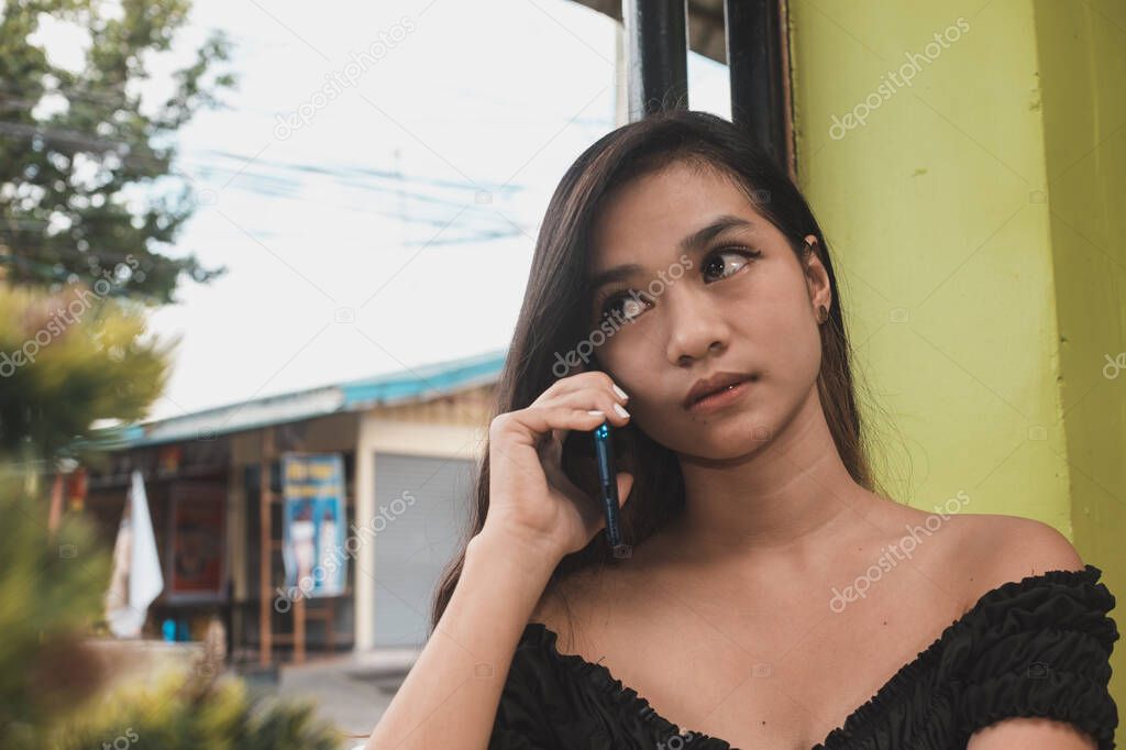 An anxious Filipina teen waits for her date or boyfriend to answer her call while waiting at a cafe.