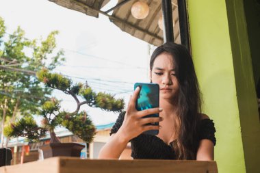 Asyalı genç bir bayan telefonda rahatsız edici bir ifadeyle bakınıyor. Al Fresk Kafe 'de.