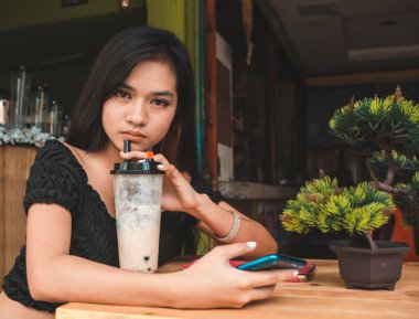 A young asian woman with a scornful and contemptuous look in her eyes, while trying to cool off with a serving of bubble tea. clipart