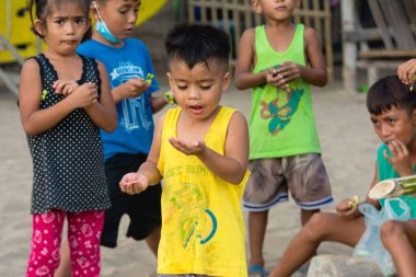 Nasugbu, Batangas, Filipinler - Mar 2021: Bir grup yerli çocuk bir plajda yerel bir köyde meyve yiyorlar.