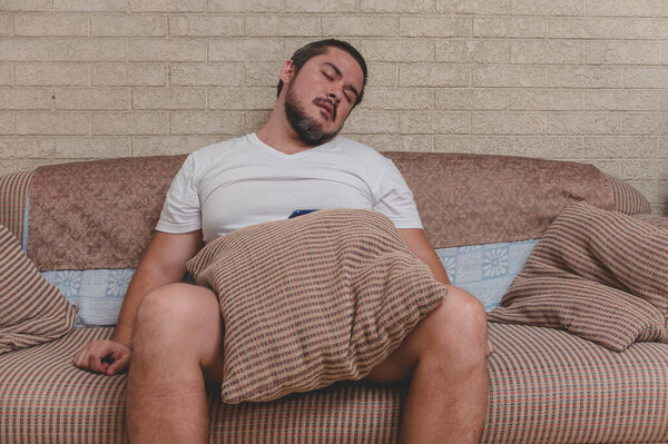 An unkempt, unmotivated and depressed man falling asleep on the couch. Exhausted from stress and other problems.