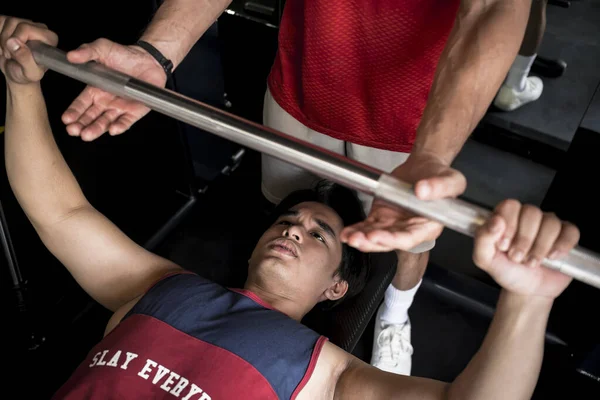 A young asian man gets a spot or assist from his training partner while doing bench presses.