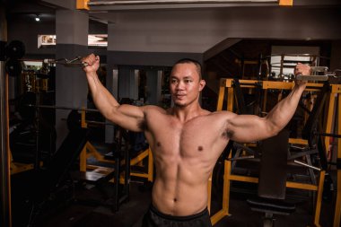 İri ve kaslı Asyalı bir adam sert bir spor salonunda çift pazılı kablo kıvırcık yapıyor. Kuvvetli bir şekilde pazı çalışıyor..