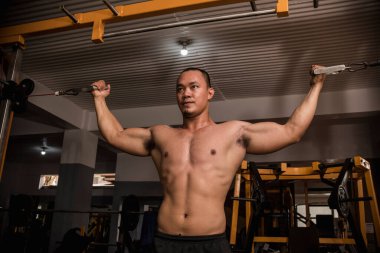 İri ve kaslı Asyalı bir adam sert bir spor salonunda çift pazılı kablo kıvırcık yapıyor. Kuvvetli bir şekilde pazı çalışıyor..
