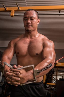 Terli, dayanıklı ve tişörtsüz Asyalı bir adam, kollarını spor salonunda bağladıktan sonra göğüs kasları kasılır ve kasılır..