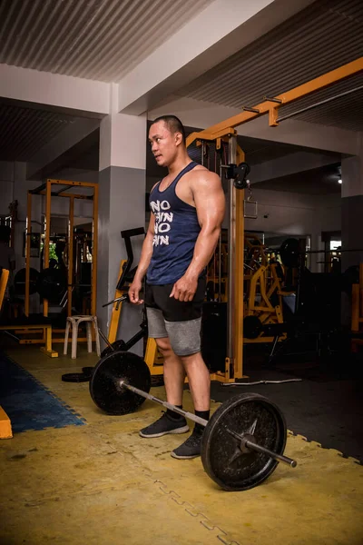 A tall, rugged and muscular man hypes himself up before doing barbell deadlifts or rows.