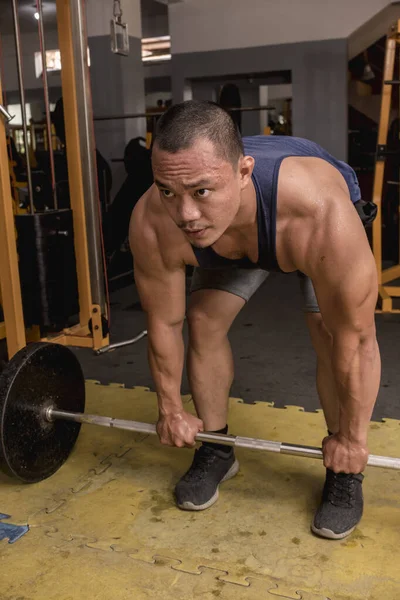 A fit, rugged and athletic asian man prepares to do barbell deadlifts, using an overhand or pronated grip. Game face and motivated.