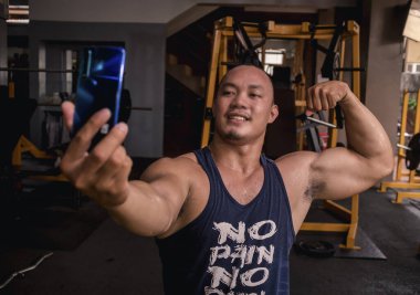 İri ve kaslı Asyalı bir adam çift pazı pozu verirken onun selfie 'sini çekiyor. Kas kazanımlarının izlenmesi veya sosyal medyaya gönderilmesi.